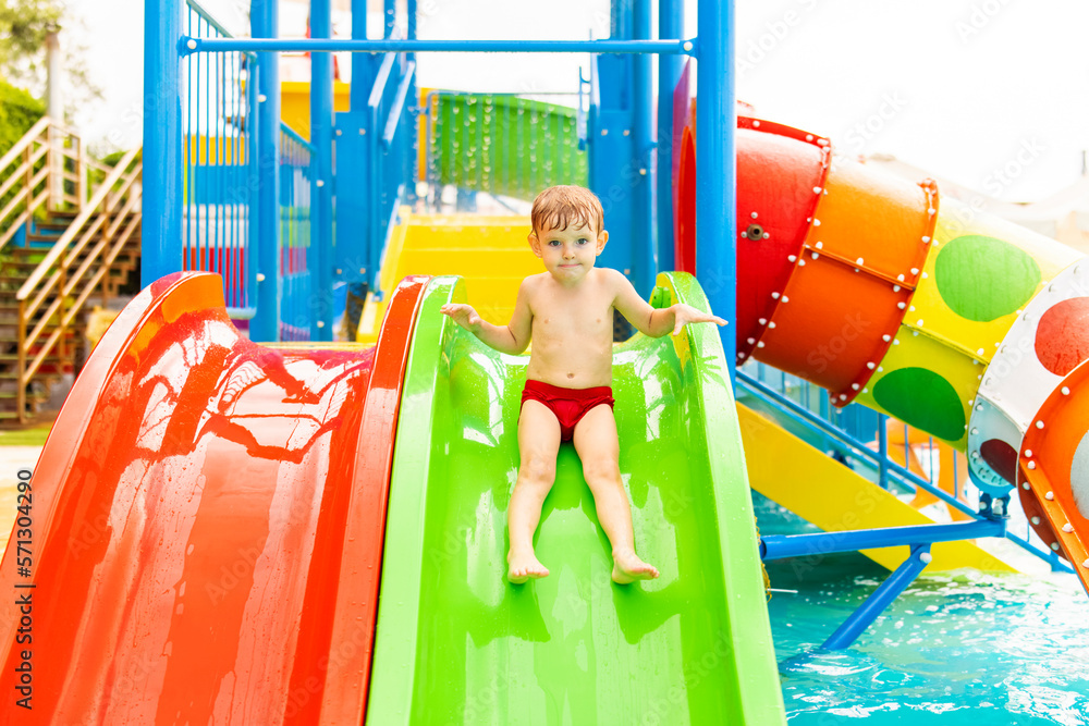 Little boy playing on water slide in outdoor pool on a hot summer day