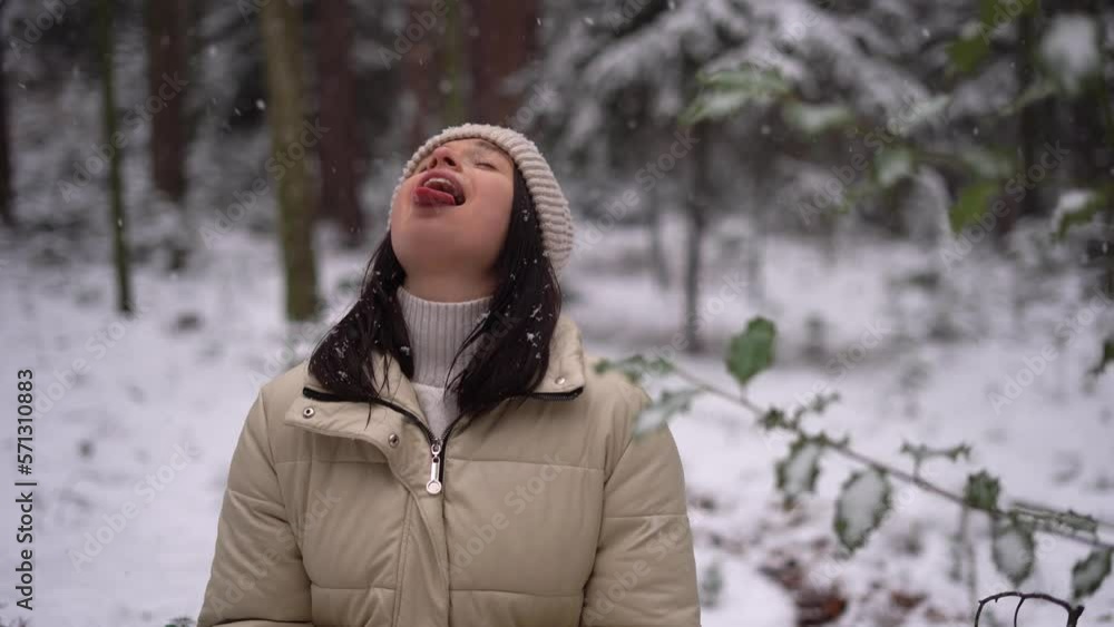 Cute girl catching snowflakes with her tongue outdoors, beige hat, Austria forest, smiling, winter Cute girl catching snowflakes with her tongue outdoors, beige hat, Austria forest, smiling, winter