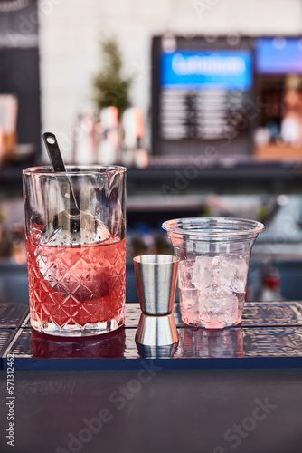 a glass bowl with ice and red liquor, a measuring glass, a jagger, a glass for a cocktail with ice stand on a blue bar stock against the background of a summer bar photo