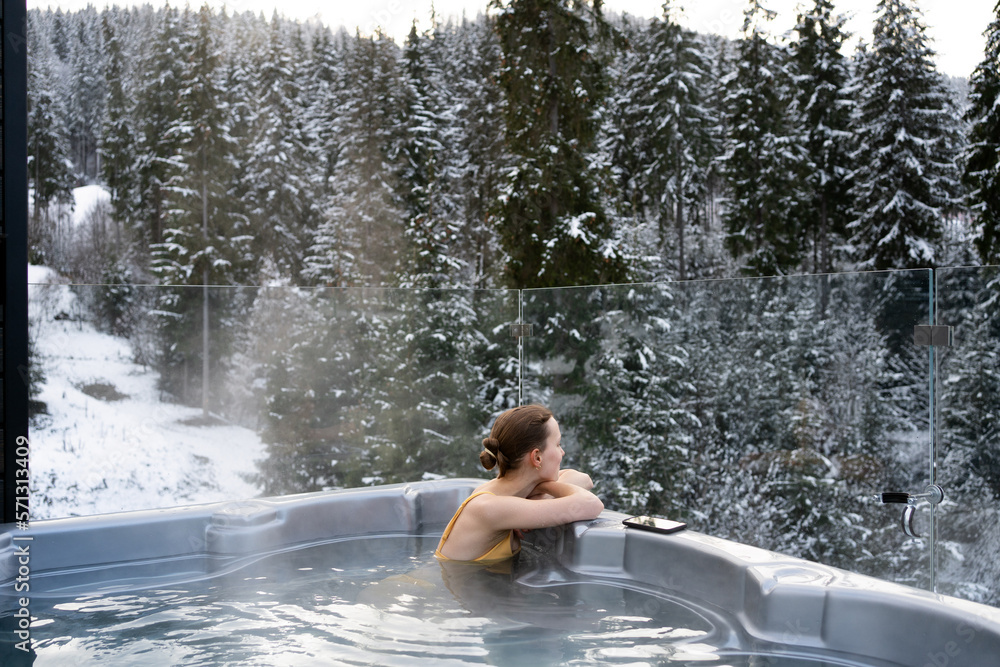 Young woman relaxing in a hot tub and thermal spa enjoying a winter view of snowy Christmas trees. Concept of recreation on hot bath and escape to nature Young woman relaxing in a hot tub and thermal spa enjoying a winter view of snowy Christmas trees. Concept of recreation on hot bath and escape to nature