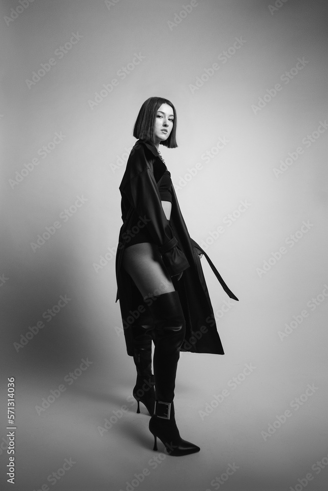 portrait of a young sexy woman in the studio on a white background in black boots and leather raincoat clothes. portrait of a young sexy woman in the studio on a white background in black boots and leather raincoat clothes.