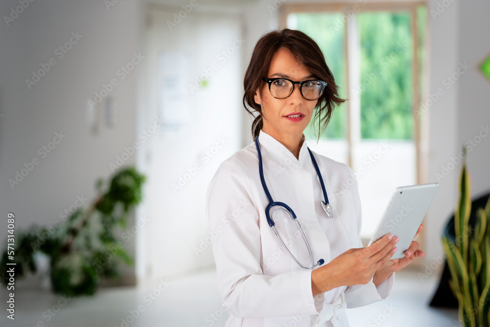 Smiling felame doctor holding digital tablet in her hand and standing at hospital foyer Smiling felame doctor holding digital tablet in her hand and standing at hospital foyer