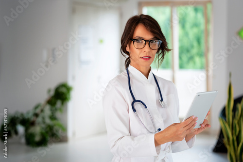 Smiling felame doctor holding digital tablet in her hand and standing at hospital foyer