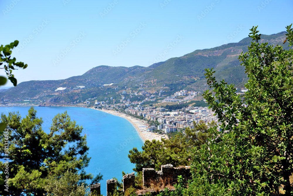 Cleopatra beach with sand line and blue water with Alanya town and mountains, topview