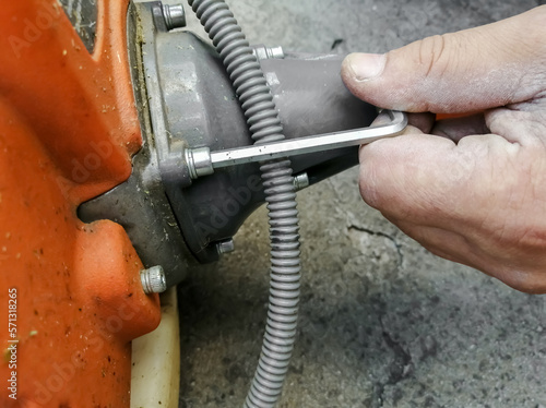 A man's hand repairs the instrument with a key. Repair of garden trimer. Key to repair the trimer motor. photo