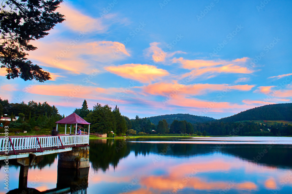 Fototapeta premium lake at sunset with soft colors in the clouds, beautiful reflection in the water, pier with viewpoint and mountains in the background, el oro de hidalgo state of mexico 