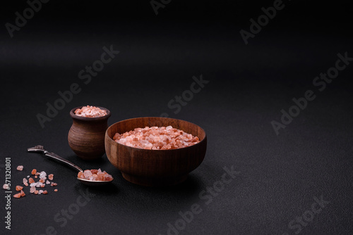 Pink himalayan salt in a wooden bowl on a dark concrete background
