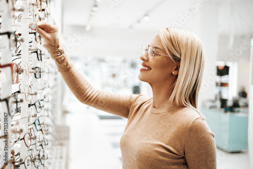 фотографія Beautiful and fashionable woman choosing eyeglasses frame in modern optical store