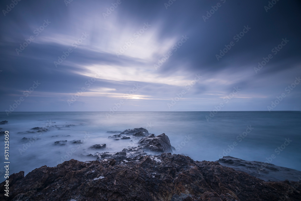 Long exposure shot of rocks on seaside, blurred and foggy sea water and clouds on sky