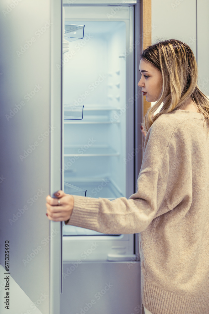 Young woman looking in empty fridge at home