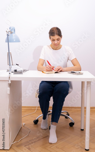 Nail beautician makes notes in notebook with pen, sitting at workstation, table in nail beauty treatment salon. Professional tools are on white table. Manicurist's routine. Vertical photo