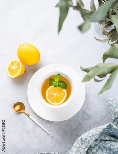 Herbal tea with lemon and mint in a white cup on a light background with eucalyptus branches and napkin. The concept of a healthy and delicious breakfast drink for immunity.