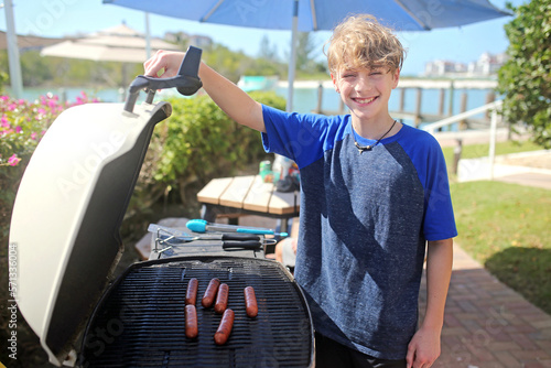 Young Teenaged Boy Cooking Hotdogs on the Grill for a Picnic for his Family photo