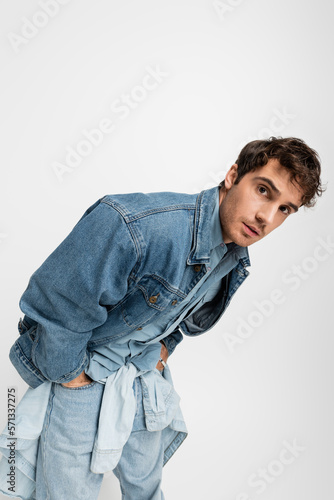 stylish young man in denim clothes posing with hands in pockets and looking at camera isolated on grey. © LIGHTFIELD STUDIOS