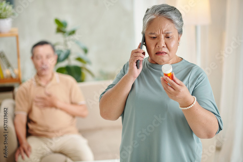 Worried senior woman calling doctor to ask if she can giving pills to husband suffering from heartache