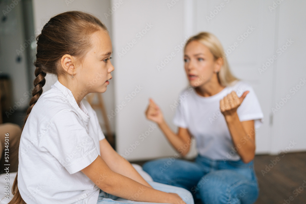 Side view of depressed little girl feeling sad to angry strict blonde mother scolding lecturing difficult kid for bad behavior at home or school. Mad mom arguing shouting at stubborn child daughter. Side view of depressed little girl feeling sad to angry strict blonde mother scolding lecturing difficult kid for bad behavior at home or school. Mad mom arguing shouting at stubborn child daughter.