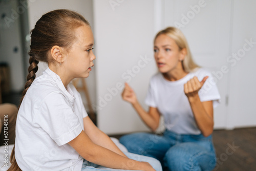 Side view of depressed little girl feeling sad to angry strict blonde mother scolding lecturing difficult kid for bad behavior at home or school. Mad mom arguing shouting at stubborn child daughter.