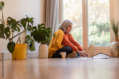 Happy mature elegant senior woman working remotely from remote home office on laptop taking notes. 60s woman using computer to watch webinar