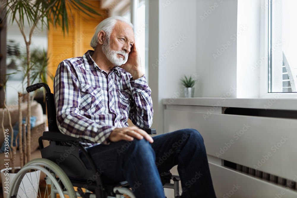 Thoughtful senior man in a wheelchair looking through window from home Thoughtful senior man in a wheelchair looking through window from home