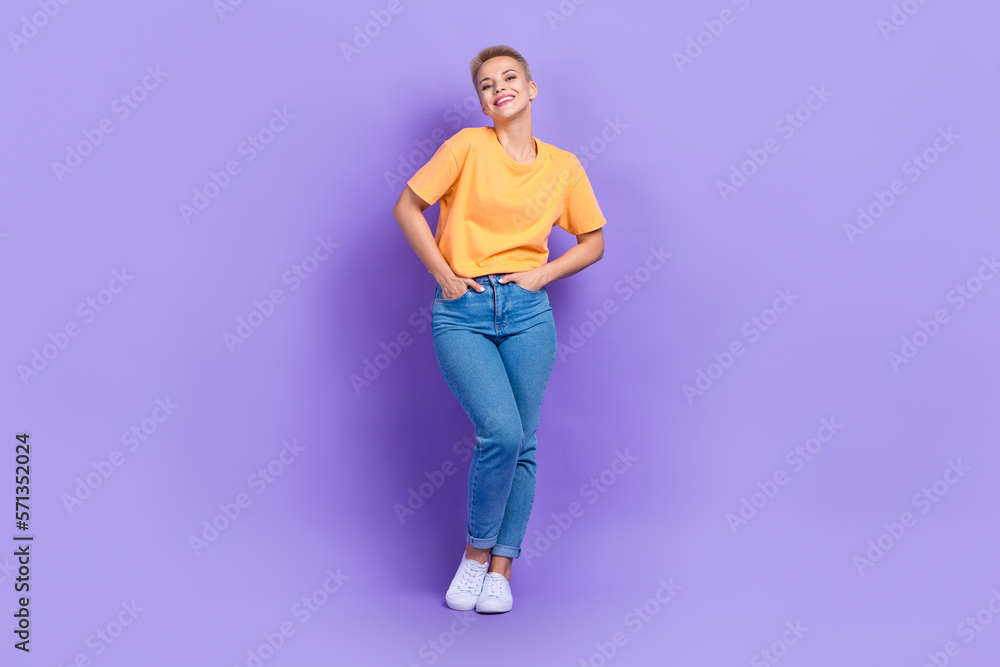 Full size photo of good mood optimistic girl dressed sneakers denim pants holds arms in pockets isolated on purple color background Full size photo of good mood optimistic girl dressed sneakers denim pants holds arms in pockets isolated on purple color background
