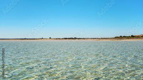 Calm sea on sunny day, tiny fishing boats in distance, sandy shore background, typical landscape at Anakao, Madagascar