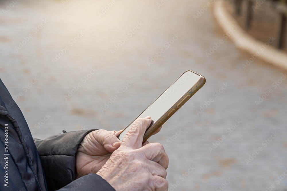 Close up, hands of old woman touching smartphone screen outside