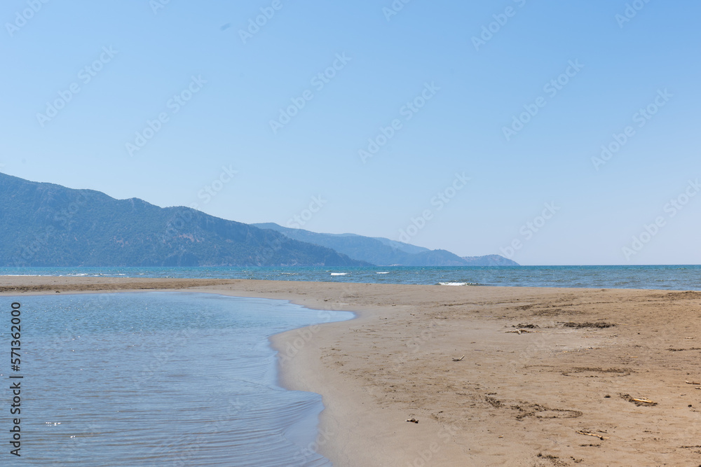 Sea beach landscape on sunny day. Blue sky, calm water and mountains. Ocean relaxing view. Selective focus