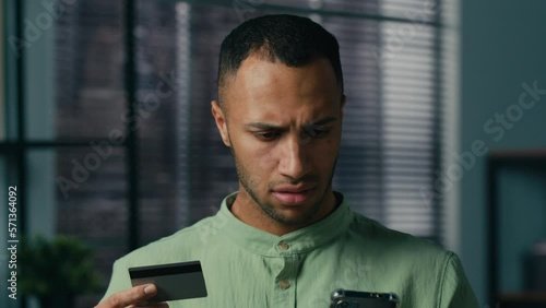 Confused puzzled african american man hold credit card try to pay using mobile banking app on phone payment error online money transfer problem blocked financial limit unsuccessful finance transaction