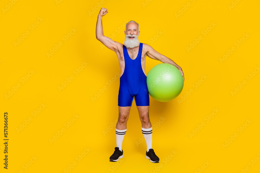 Full body size photo old retro senior grandfather hand up celebrate hold fitball acrobatics wear blue sportswear excited hooray isolated on yellow color background