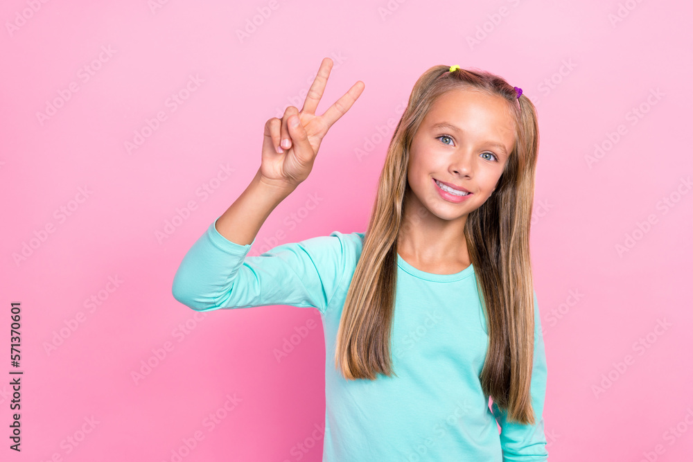 Closeup photo of young little preteen schoolkid girl wear blue shirt toothy smile showing v-sign hello greetings hello isolated on pink color background Closeup photo of young little preteen schoolkid girl wear blue shirt toothy smile showing v-sign hello greetings hello isolated on pink color background