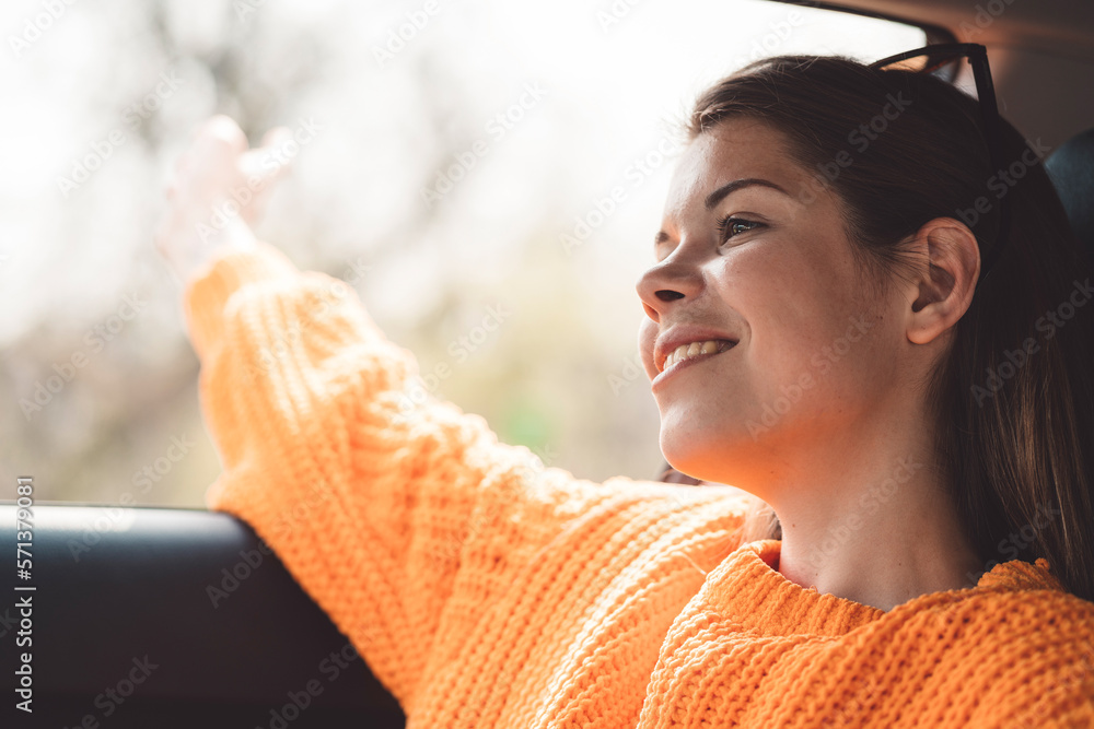Side portrait waist up young woman sitting in her car looking out the window with a smile on her face Side portrait waist up young woman sitting in her car looking out the window with a smile on her face
