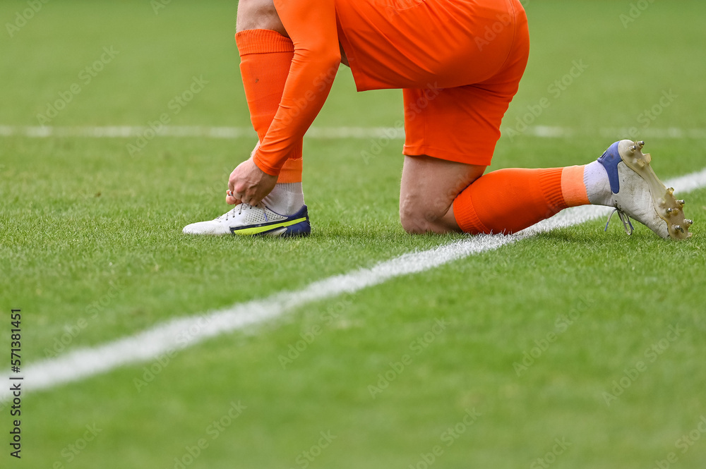 Obraz premium The football player itying his shoe on the turf of the pitch