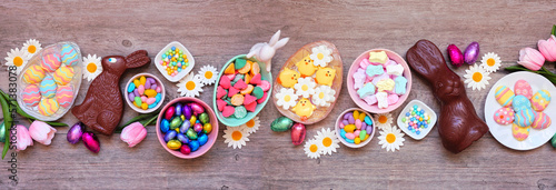 Easter candies. Overhead view table scene on a wood banner background. Chocolate bunnies, candy eggs and a collection of sweets.