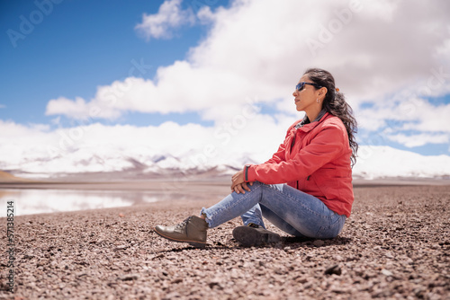mujer latina contemplando laguna entre montañas nevadas de los Andes © Juan