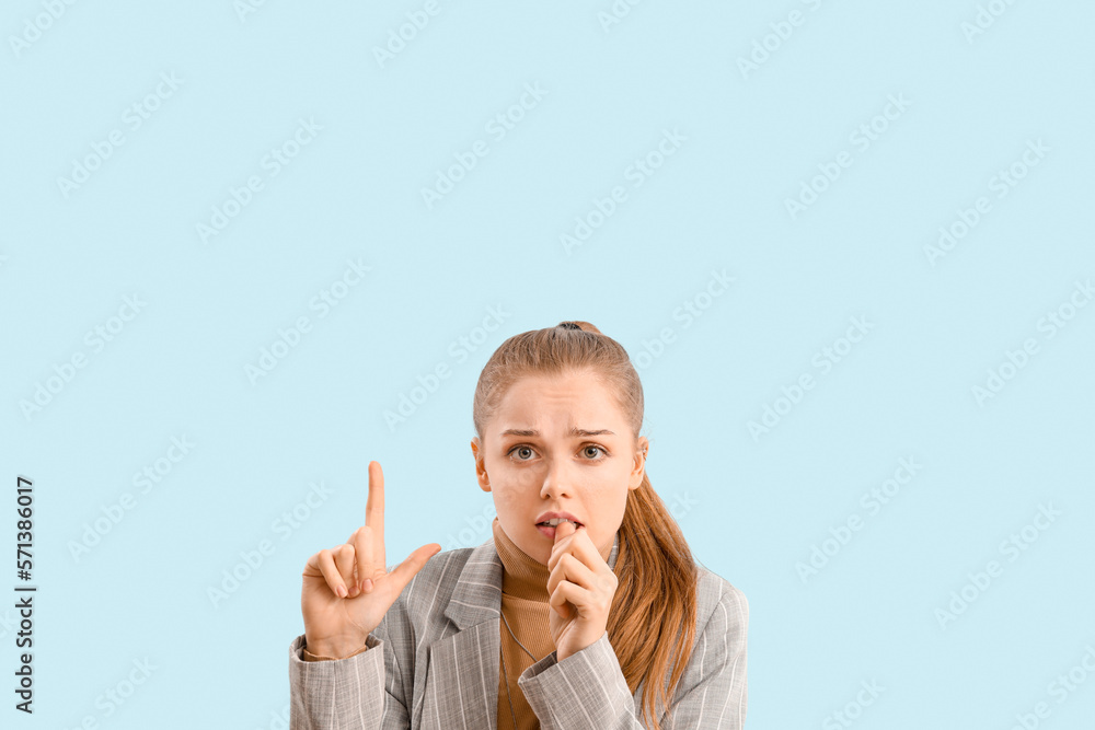 Young businesswoman biting nails and pointing at something on blue background Young businesswoman biting nails and pointing at something on blue background