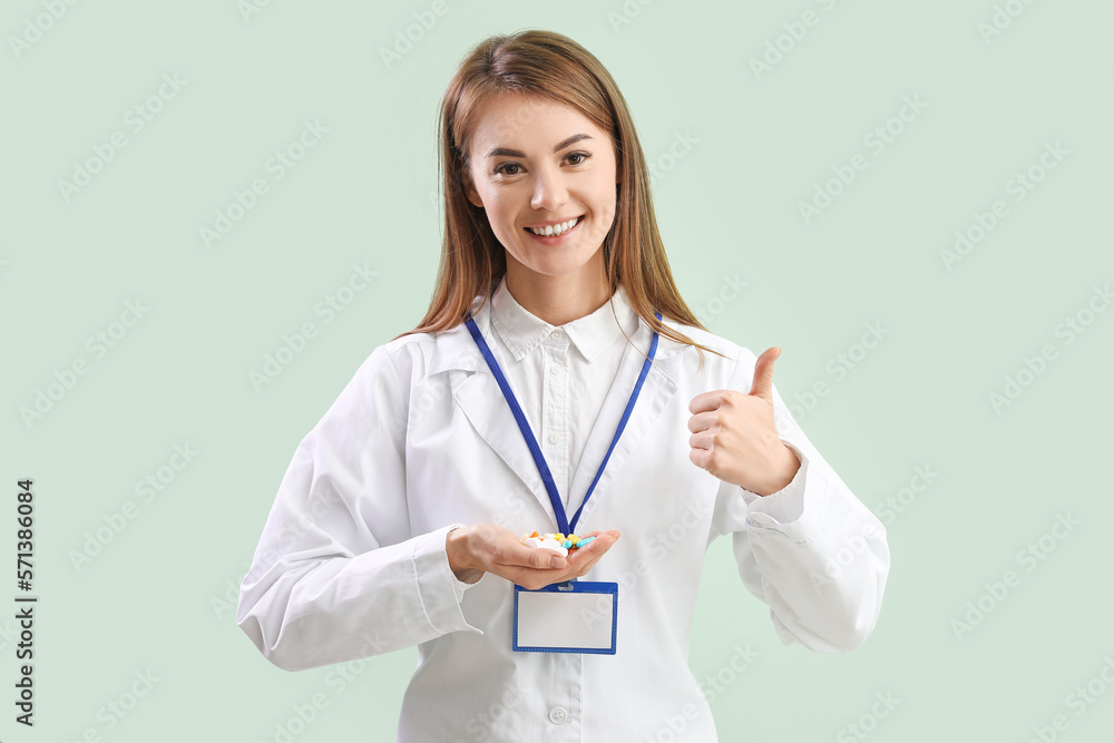 Female doctor with pile of vitamin supplements showing thumb-up on green background Female doctor with pile of vitamin supplements showing thumb-up on green background