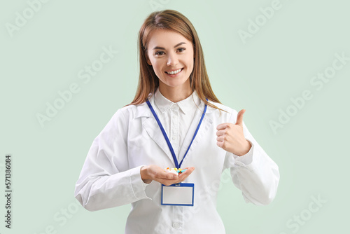 Female doctor with pile of vitamin supplements showing thumb-up on green background