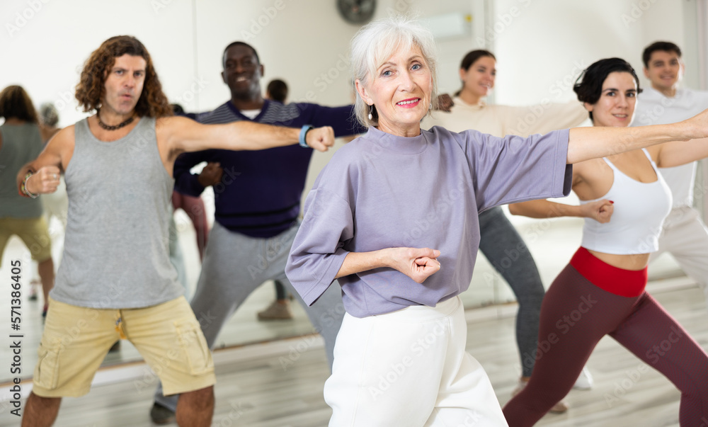Happy mature woman practising modern dance moves with other people in dance studio