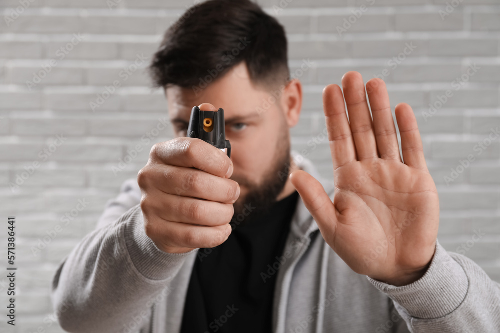 Young man with pepper spray for self-defence showing STOP gesture on grey brick background, closeup Young man with pepper spray for self-defence showing STOP gesture on grey brick background, closeup