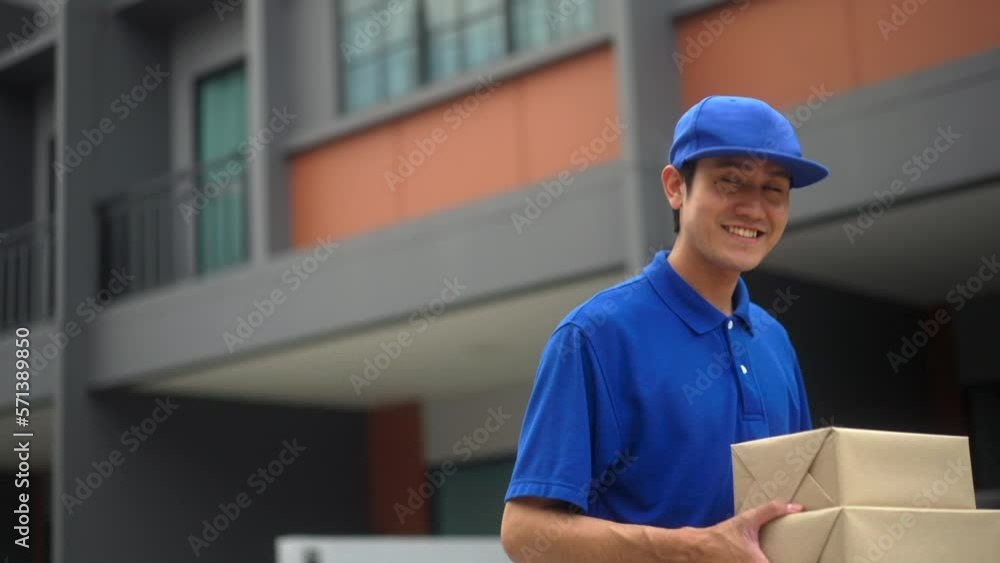 Blue uniform delivery handsome man walk and send parcel to customer front of the house with good service from shopping online. Courier man delivering a cardboard box postal package to destination. Blue uniform delivery handsome man walk and send parcel to customer front of the house with good service from shopping online. Courier man delivering a cardboard box postal package to destination.