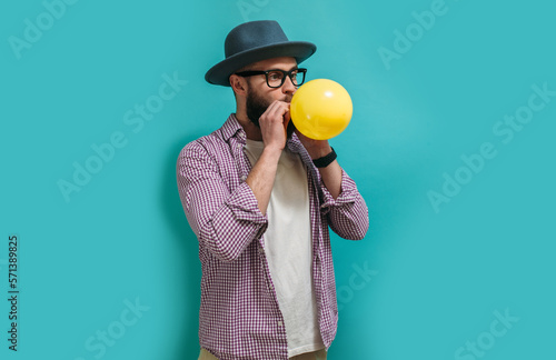 Portrait of a funny hipster guy inflating a balloon. Happy birthday concept, celebration, party. Crazy emotions. Discounts, sales, seasonal sales. Colorful summer concept.