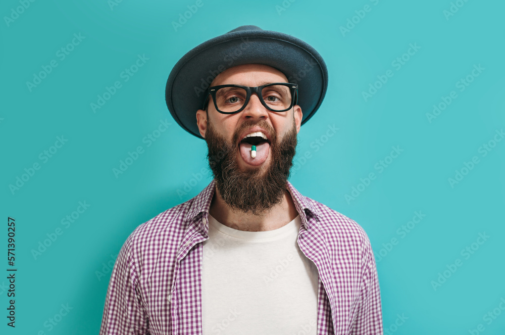 A handsome man in casual clothes with a beard in glasses takes colorful pills. Drug pill on the tongue A handsome man in casual clothes with a beard in glasses takes colorful pills. Drug pill on the tongue