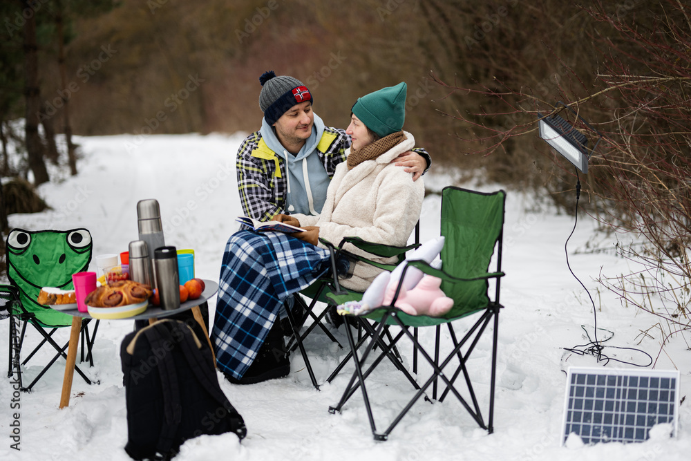 Couple in love sit in chair and read book in winter forest on a picnic.