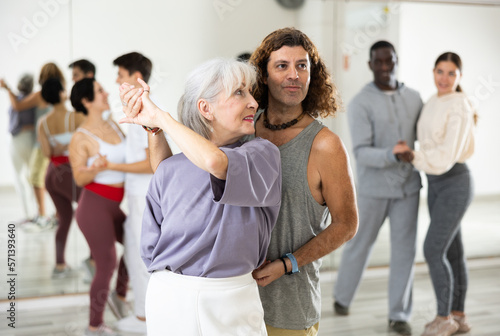 Positive elderly woman enjoying dancing in pair with expressive man during group training in dance studio