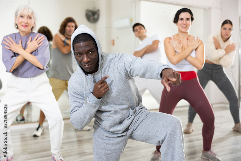 Fototapeta premium Cheerful adult African American man learning to dance krump with group in modern choreographic studio