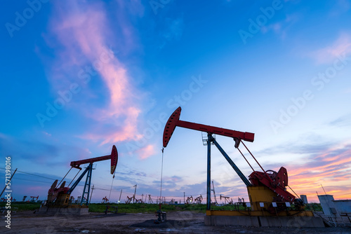 in the evening, oil pumps are running, The oil pump and the beautiful sunset reflected in the water, the silhouette of the beam pumping unit in the evening.