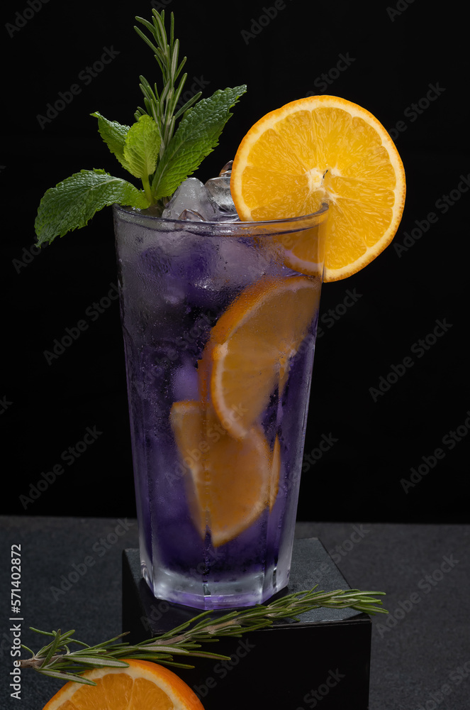 Fototapeta premium a purple cocktail glass decorated with orange and mint on a dark background