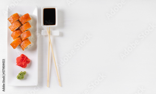 Sushi roll Philadelphia with salmon, avocado, cream cheese on white background. Sushi menu, rolls served on white dish with wasabi, ginger and soy sauce. Japanese cuisine food. Banner, copy space