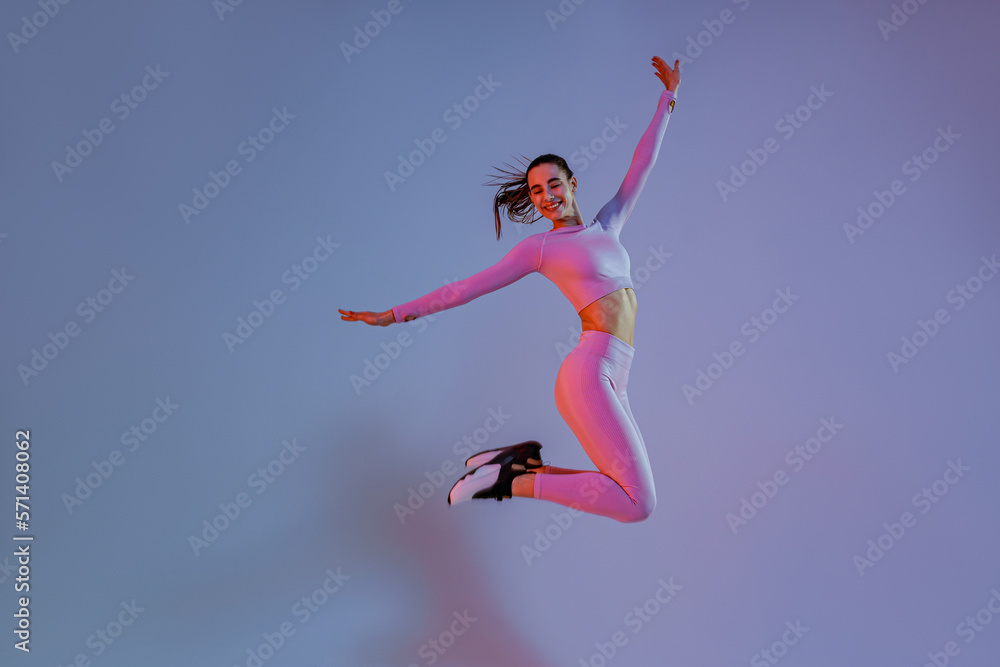 Athletic active woman jumping on studio background with colored filter. Dynamic movement Athletic active woman jumping on studio background with colored filter. Dynamic movement