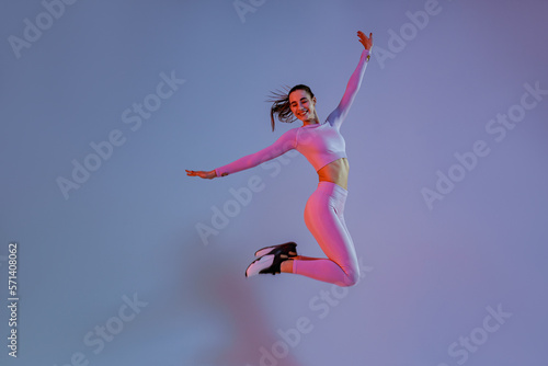 Athletic active woman jumping on studio background with colored filter. Dynamic movement © Yaroslav Astakhov